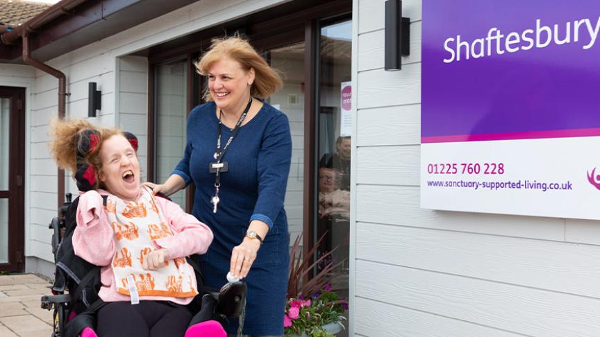 Smiling staff member and resident, who is a wheelchair user, outside of the Shaftesbury Court main entrance