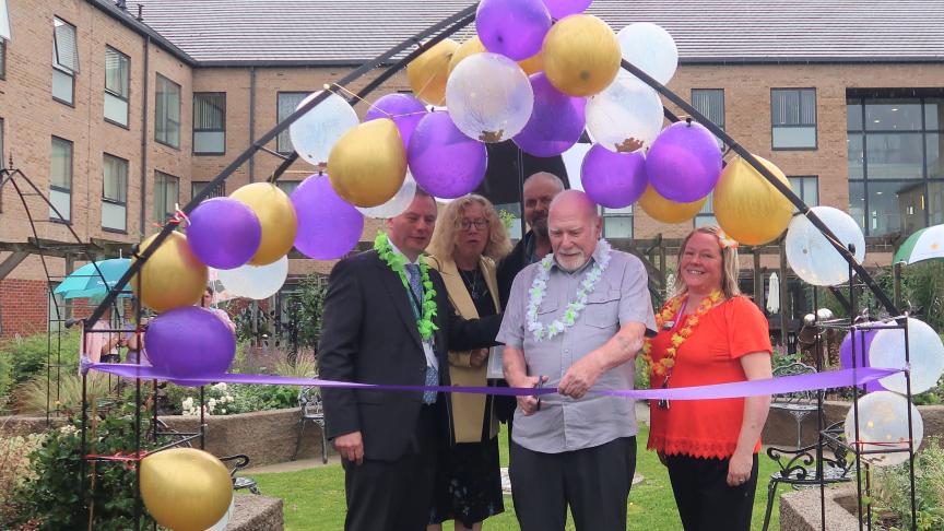 Craig Moule and members of staff at Baskeyfield House in the new memorial garden at Baskeyfield house stood under some purple balloons with one of them cutting a purple ribbon
