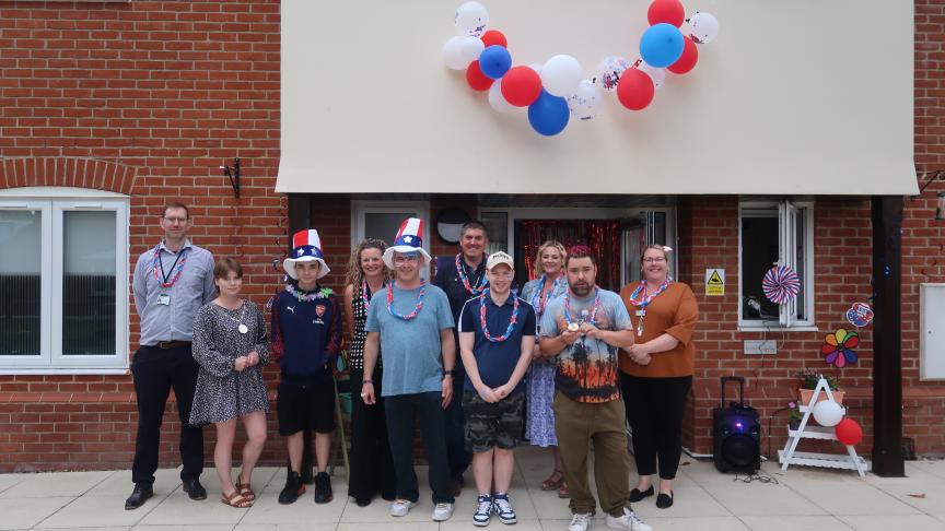 Staff and residents stood outside Oak Lodge and Laurea House with some wearing red white and blue hats and others wearing garlands with red white and blue balloons hanging behind them