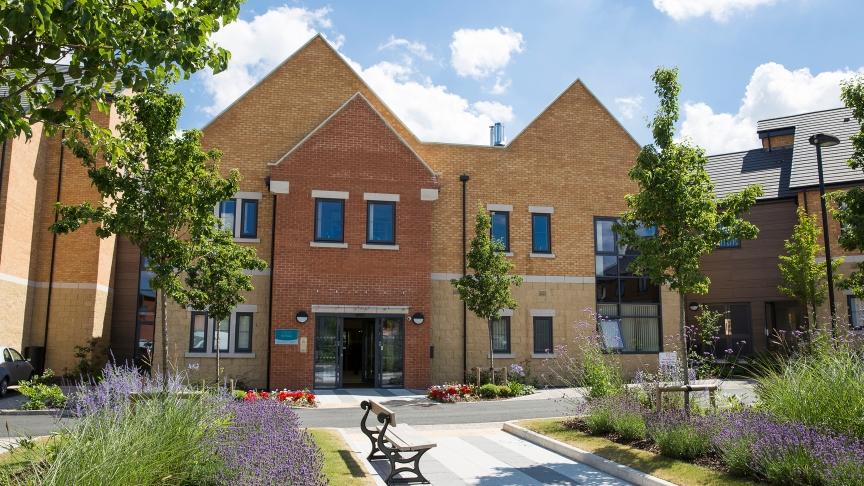 Exterior image of Noble House, a modern building with large windows and a beautiful garden with luscious green grass, trees and colourful flowers
