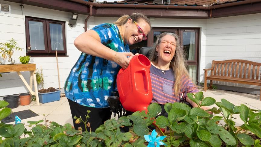 SSL staff member and resident in the garden on a sunny day watering plants with a watering can