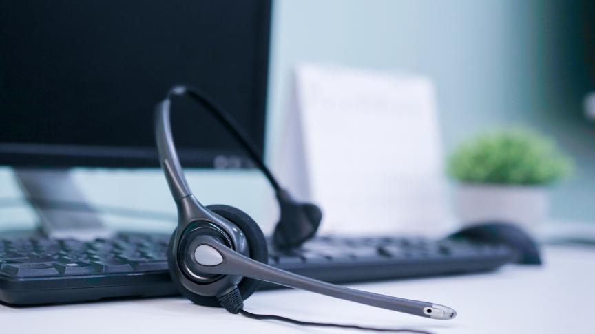 Close up of a telephone headset on top of a black computer keyboard with a monitor in the background