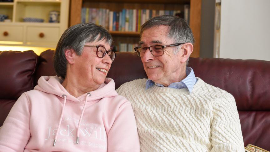 Two people wearing cosy jumpers looking into each other's eyes while sitting on a dar red sofa
