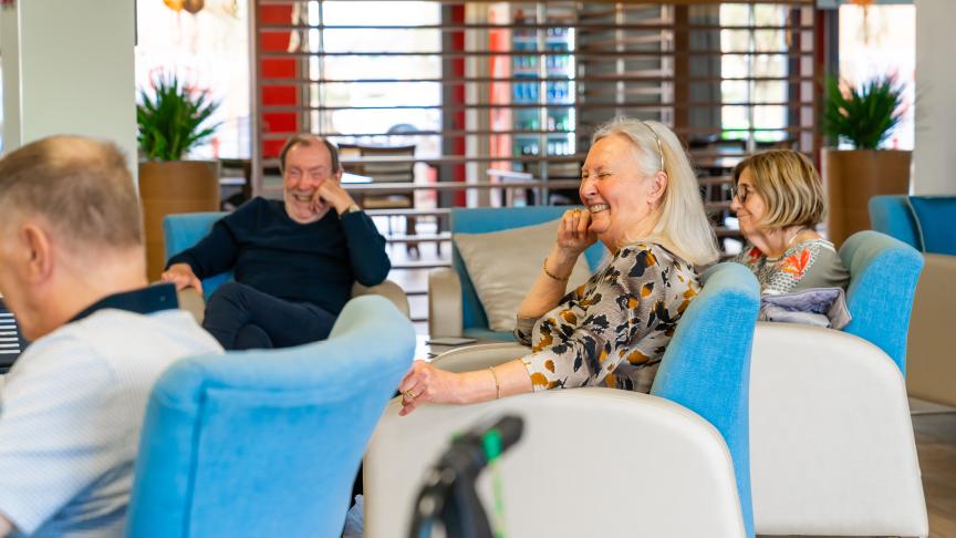 4 residents are seated in a communal area laughing and smiling
