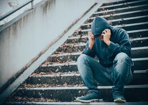 Stock image of a young man sitting on some steps holding his head in his hands