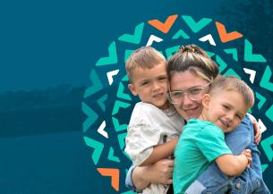 A young woman with glasses is smiling and hugging two young boys, one on each side