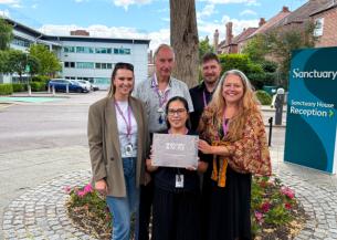 Five Sanctuary colleagues standing outside Sanctuary House holding an Investors in People Platinum accreditation plaque