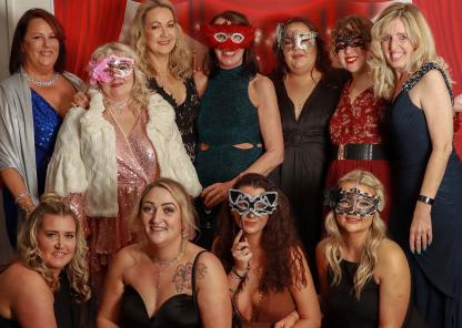 TDAS staff posing for a photograph in their glamorous outfits at a masquerade ball to raise money in support of their work. Several of the ladies pictured are wearing glittery masks.