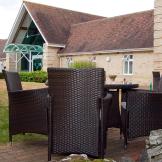 Two outdoor charcoal wicker dining sets are placed amongst the bricked walkways surrounding the grassed area. 