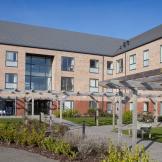 Stylized retirement living community with an array of large windows over looking a sectioned off grassed areas, flower beds and walkways, located in Stoke-on-Trent.