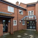 Multi-entranced brick exterior with terracotta clay roof tiles. Multiple security cameras and lighting. Accessed by a clean concrete tiled walkway to Drawbridge House.