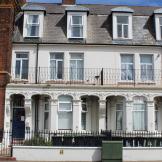 Ornate exterior of a three-storey whitewashed terraced supported housing property in Great Yarmouth. With second storey property width balcony.