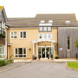 A modern two storey property built with yellow brick and a wooden panelling in random locations on the exterior of the property. The entrance has a covered walkway and dropped curb access. 
