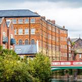 Riverside view of Kelham Island museum in Sheffield, and colourful green, red and white bridge spanning the river. 