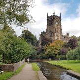 Canal footpath with grass verge and an array of mature trees with a 15th century church towering above.