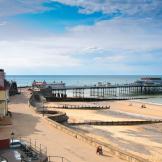 Large promenade walkway leading to a modern pier which features over a mixture of sand and stone beach and into the North Sea.