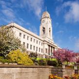 Stone built town hall with well-maintained gardens in bloom.