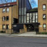 Traditional yellow brick built apartment block, featuring dark brown wooden panelling on the entrance elevation and window panes. 