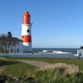 Picturesque red and white striped lighthouse on the edge of the cliff face, behind sits numerous joined buildings to facilitate the lighthouse.