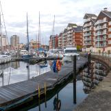 Multiple docked yachts on the waterfront with the city skyline in the distance and modern apartments built around the waters edge.