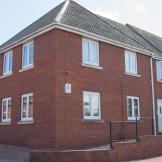New build, red brick corner plot with new white PVC windows, doors and garage. A bricked wall surrounds the walkways. 