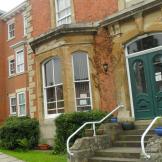 Victorian styled, three storey property with protruding bay windows and an array of forest green and red double entrance doors. 