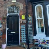 A very homely array of items adorn the outside of the Victorian styled property. Teal blue painted wall trellising and personalised plaques are placed around the doorway and as a separation between the neighbouring property.