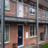 Industrial support metal beams and balcony on the second storey frame the entry to Thomas Court flats. 