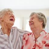 Two happy elderly women embracing each other at home