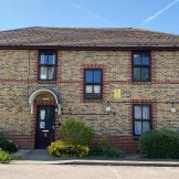 Traditional, elongated, two storey brown bricked property with decorative red brick design around the windows and entrance door. Small, well maintained shrubbery lines the perimeter of the property.