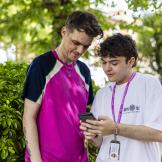 A Sanctuary Supported Living employee and a young male stood together looking at a phone outside in the sunshine