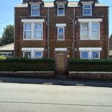 A 3 story dark brown brick building with white window panes. A hedge surrounds the front perimeter with a gap in the middle to allow entry