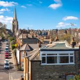 Residential street lined with Victorian houses and a church spire under a blue sky.
